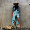 Eine Frau in einem blau-tiegedyedeten Kimono-Überkleid und Strohhut vor einer strukturierten grauen Wand.