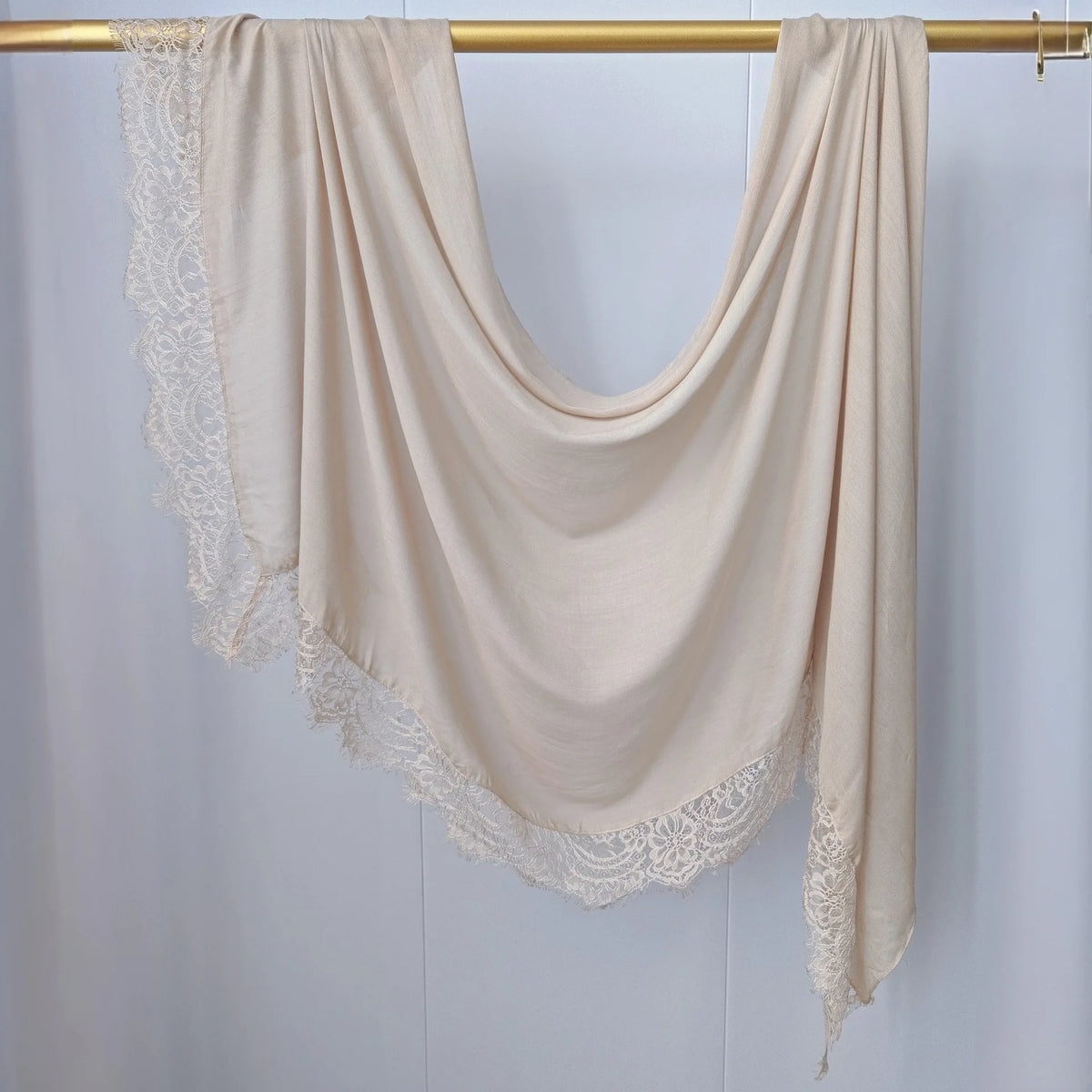 Hijab de malla beige con estampado doble, drapeado sobre un perchero de madera.