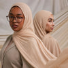 Une femme portant un foulard modal beige et des lunettes, regardant sur le côté.