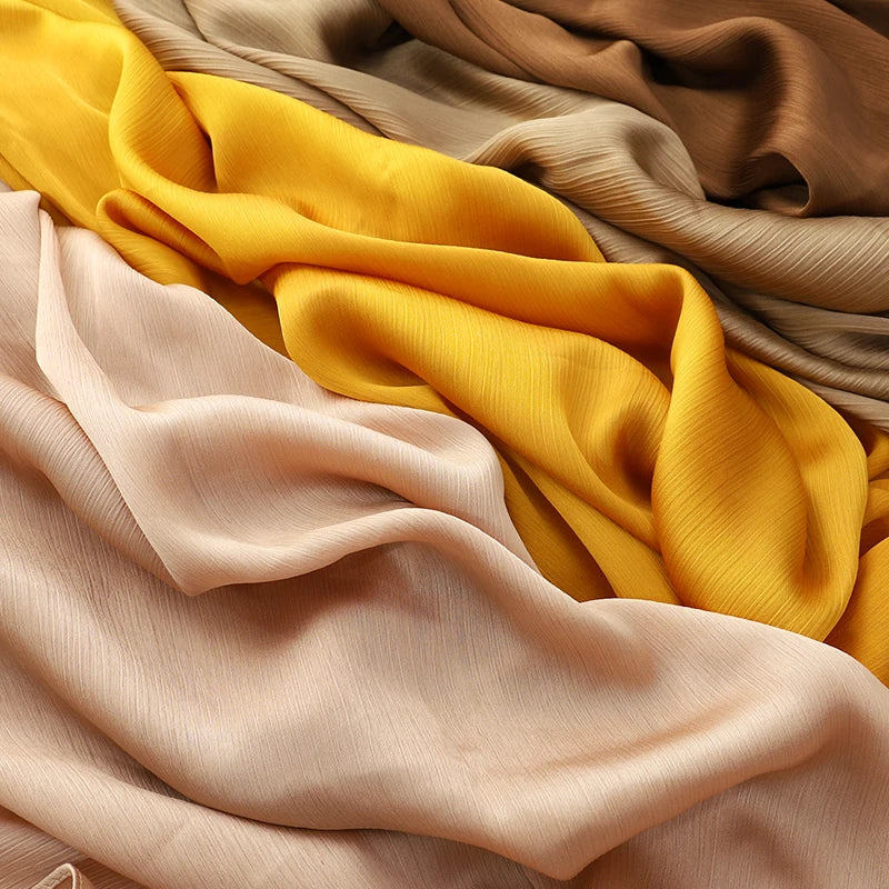 Nahaufnahme mehrerer drapierter Satin-Crinkle-Hijabs in Gelb-, Beige- und Nude-Tönen.