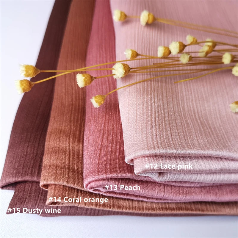 Stapel von Crinkle-Satin-Chiffon-Hijabs in Rosa-, Pfirsich- und Weinfarben mit goldenen Blumenakzenten.
