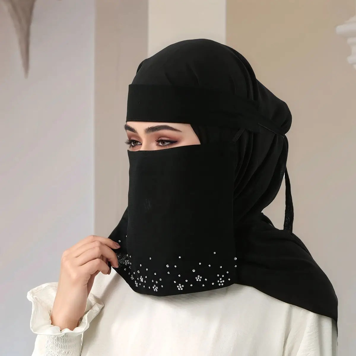 Eine Frau trägt einen eleganten schwarzen Face-Veil-Hijab mit floralen Diamantverzierungen und einem weißen Oberteil.