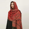 Una mujer modela un pañuelo pashmina de lujo con estampado rojo y dorado sobre su cuello.