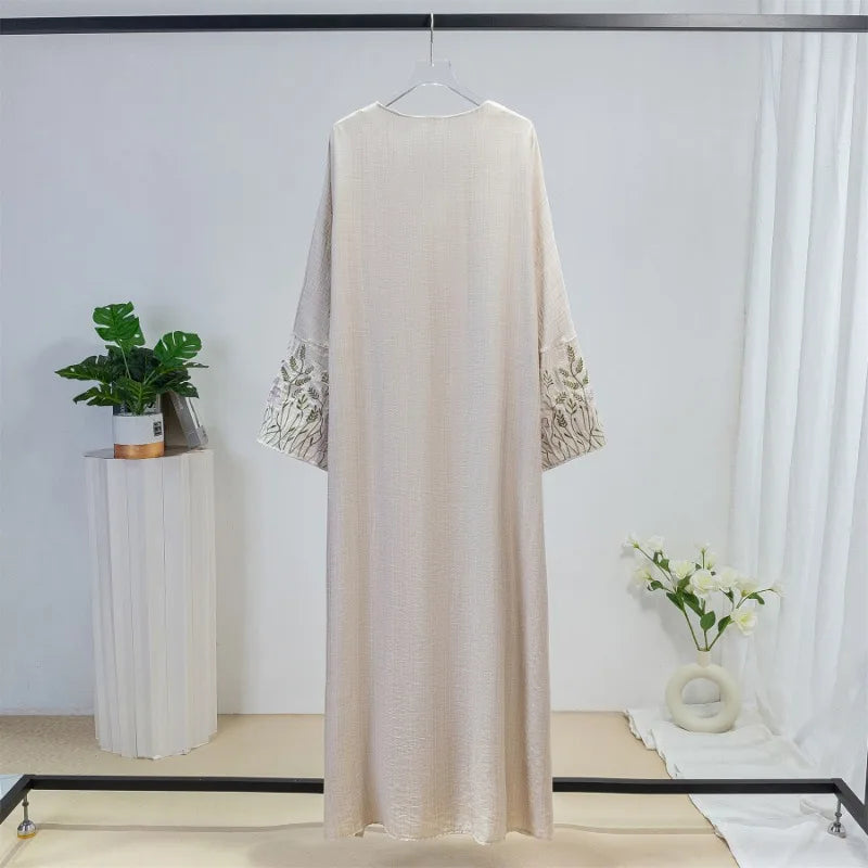 Beige bestickte, lockere Kaftan-Abaya an einem Haken vor einer weißen Wand.