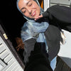Eine Frau trägt einen blauen Aquarell-Hijab und dunkle Kleidung und lächelt nach unten.