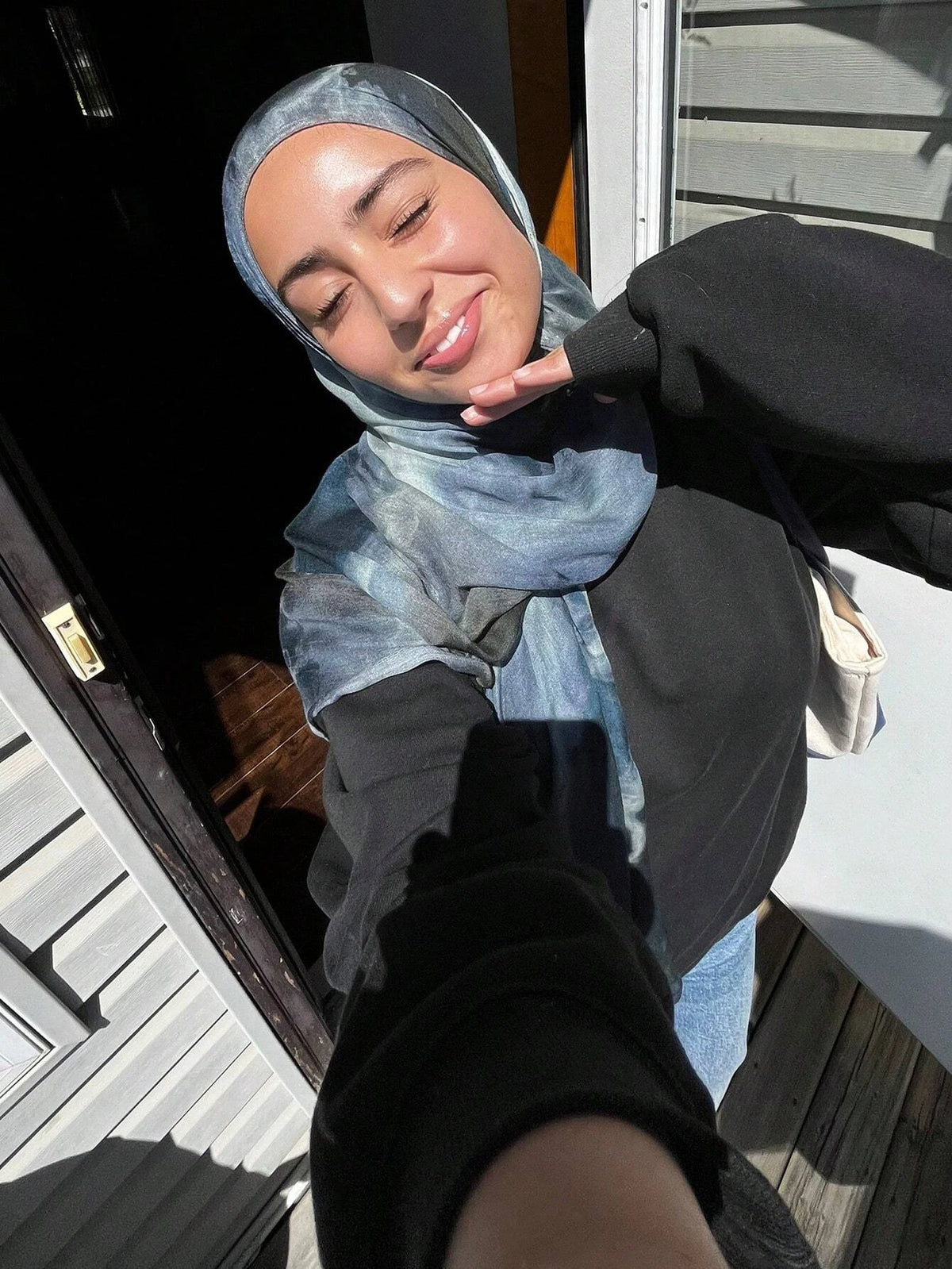 Eine Frau trägt einen blauen Aquarell-Hijab und dunkle Kleidung und lächelt nach unten.