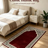 Un tapis de prière islamique rouge foncé et noir exposé sur un parquet clair à côté d'un lit.