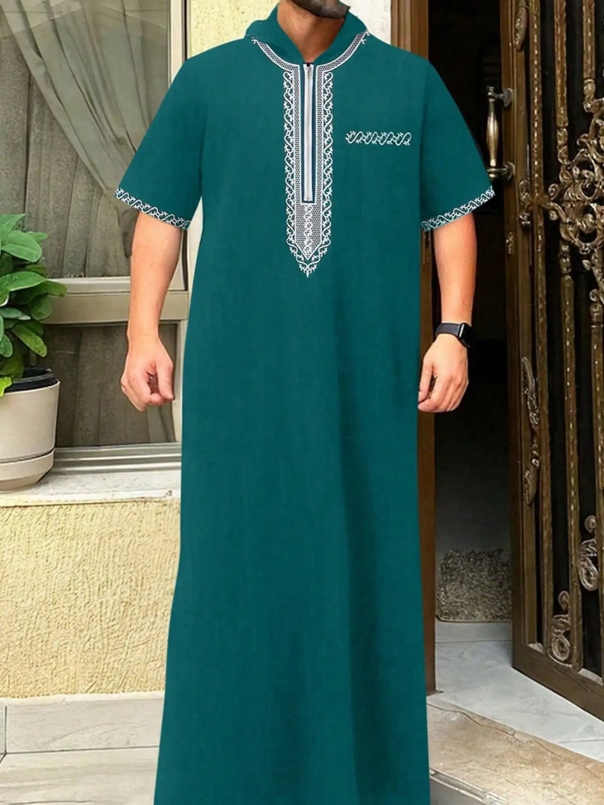 A dark teal Moroccan men's ethnic thobe with a stand collar and white embroidery, displayed in an entryway.