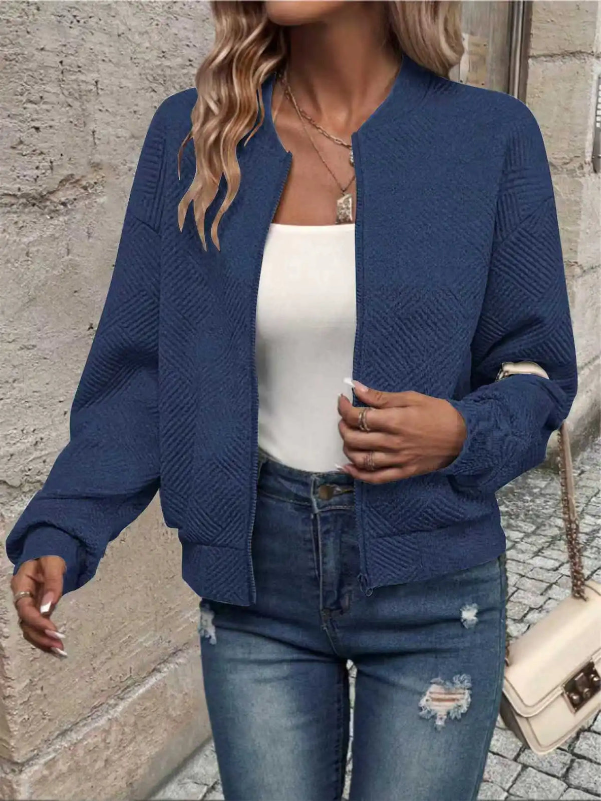 Une femme portant une veste à fermeture éclair bleu marine sur un haut blanc et un jean bleu.
