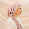 A woman wearing a solid color pink turban hijab cap and white top, shown in profile.