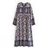 A long bohemian floral maxi dress in navy blue with intricate gold and cream patterns and lantern sleeves.