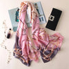 Pinkes und lila Pfauenfederschal aus Seide, drapiert neben einer schwarzen Clutch und einer Zeitschrift.