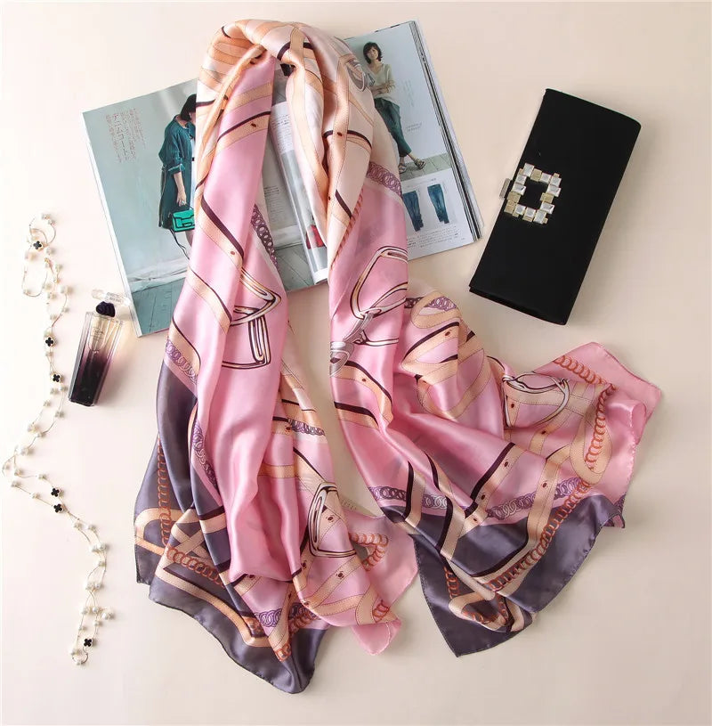 Pinkes und lila Pfauenfederschal aus Seide, drapiert neben einer schwarzen Clutch und einer Zeitschrift.