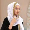 Eine Frau trägt einen weißen Spitzen-Chiffon-Hijab mit goldener Stickerei und einem schwarzen Oberteil.