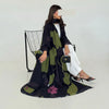 Una mujer modela un conjunto de abaya de gasa negra y verde oliva con pantalones blancos y joyas de oro.