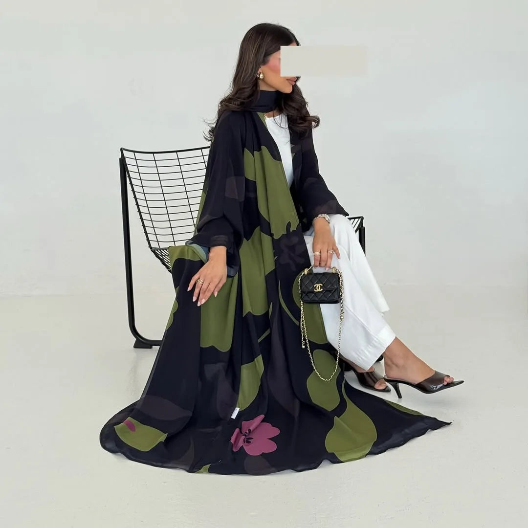 Una mujer modela un conjunto de abaya de gasa negra y verde oliva con pantalones blancos y joyas de oro.