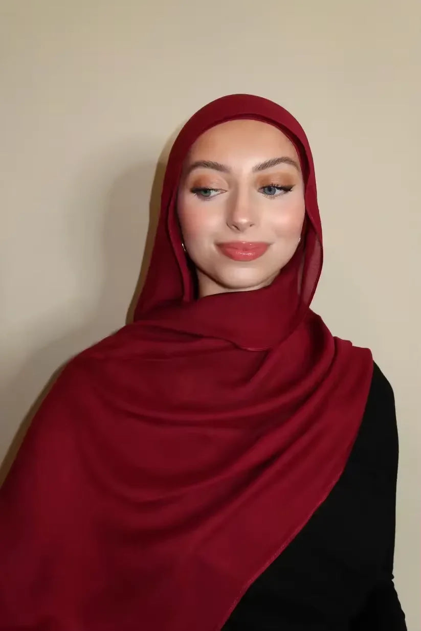 Eine Frau trägt einen tiefroten Gradient-Rayon-Modals-Hijab und schwarze Kleidung.