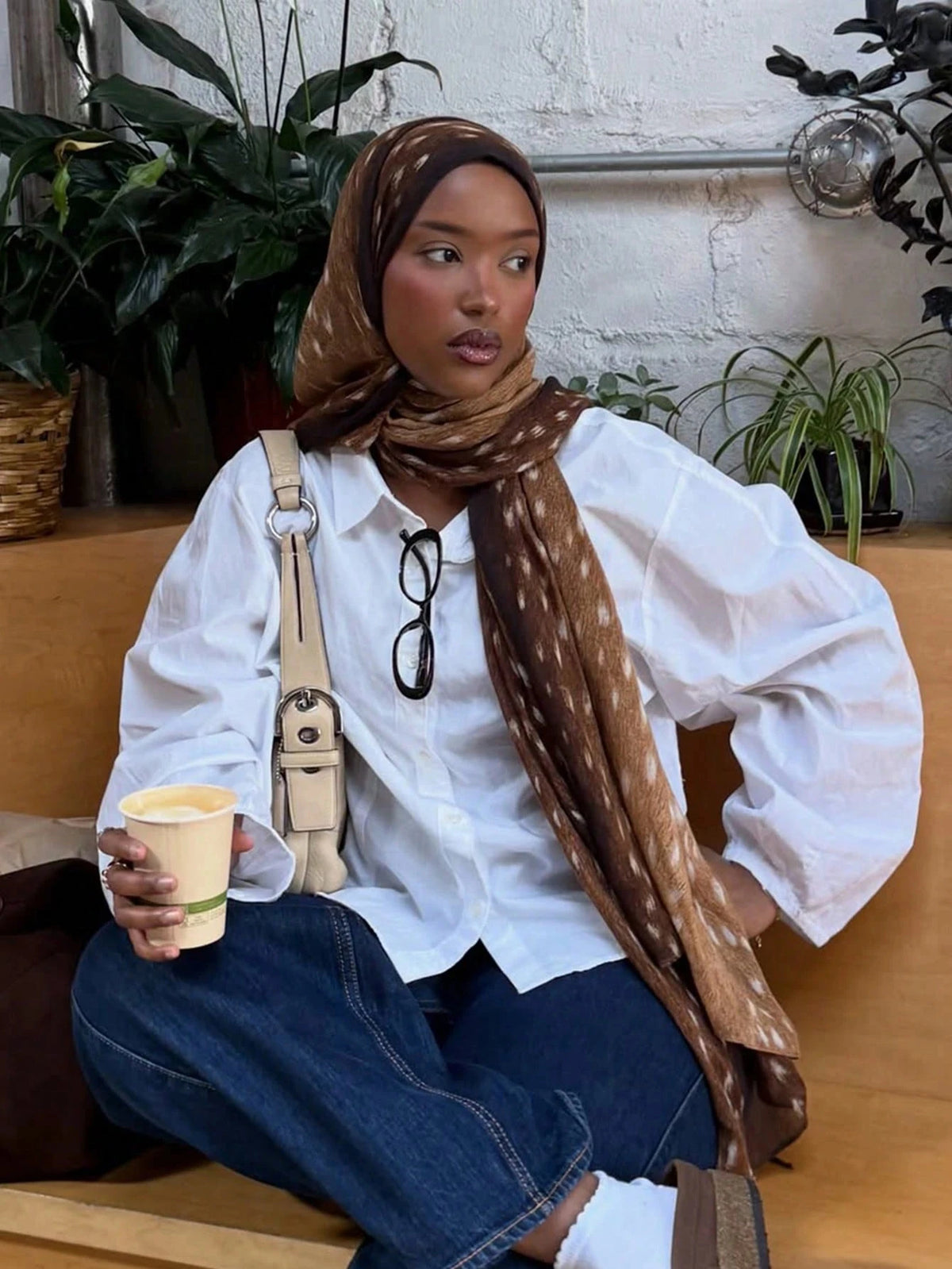 Eine Frau mit weißem Shirt und blauen Jeans und einem braunen Aquarell-Hirschmuster-Hijab-Schal.