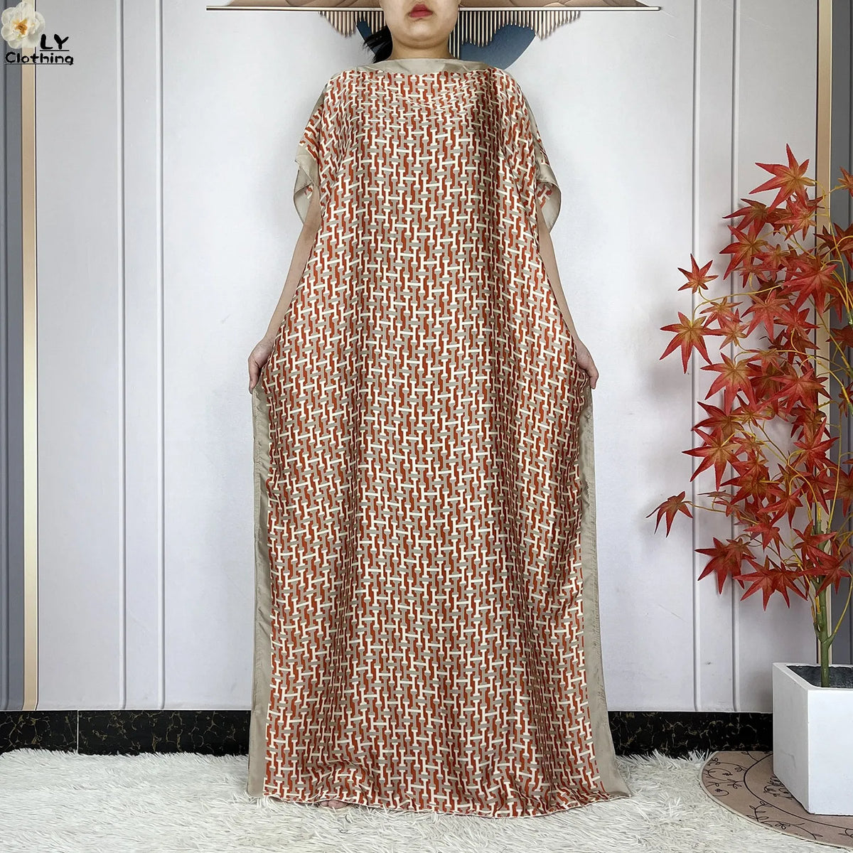 Eine Frau trägt ein fließendes, rotbraun gemustertes Kaftankleid mit hellem Beige-Zier