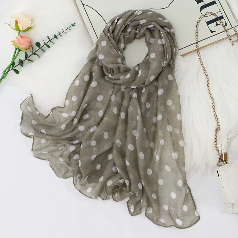 Ein weicher grauer, durchscheinender Schal mit weißen Polkadotten elegant über einer weißen Oberfläche drapiert.