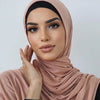Eine Frau trägt einen staubrosa Baumwoll-Jersey-Schal und einen schwarzen Hijab und blickt direkt in die Kamera.