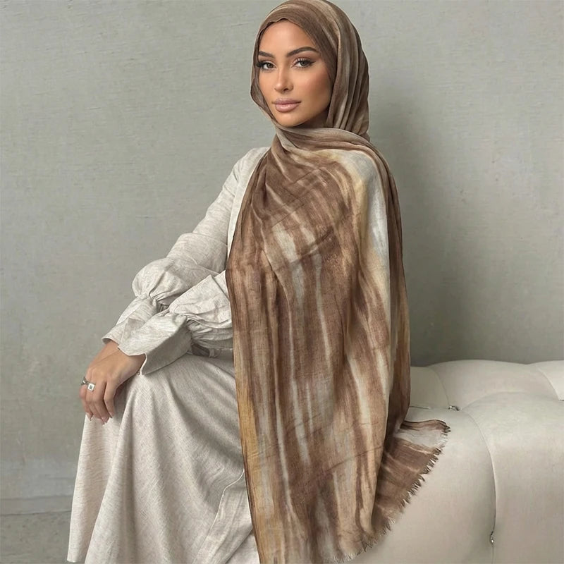 Una mujer vistiendo un pañuelo hijab estampado en acuarela marrón y beige con un vestido blanco.
