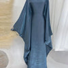 Una abaya de satén azul polvoriento y fluido con corte batwing, drapeada en un maniquí.