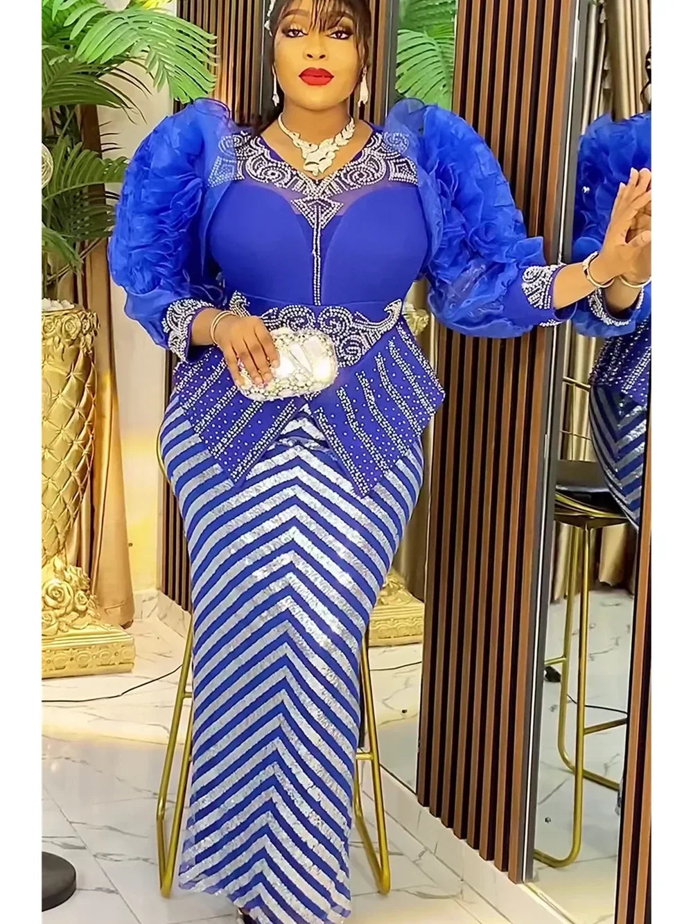 A woman wearing a royal blue sequin African party dress with sheer blue sleeves and gold jewelry.