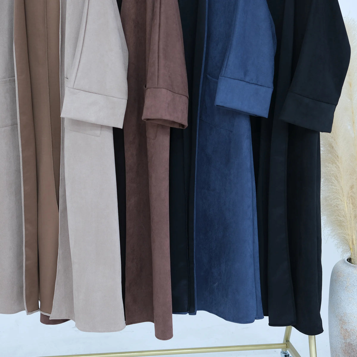 A display of elegant women's abaya trench coats in various neutral and dark tones.