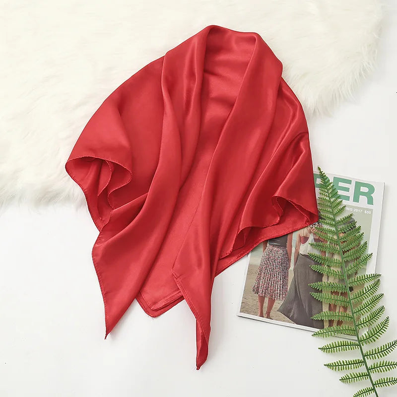 A vibrant red silk satin hijab scarf draped over a white fluffy surface.