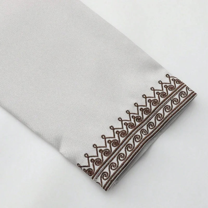 Primer plano de una túnica casual de jubba bordada gris claro para hombre con detalles de ribete marrón.