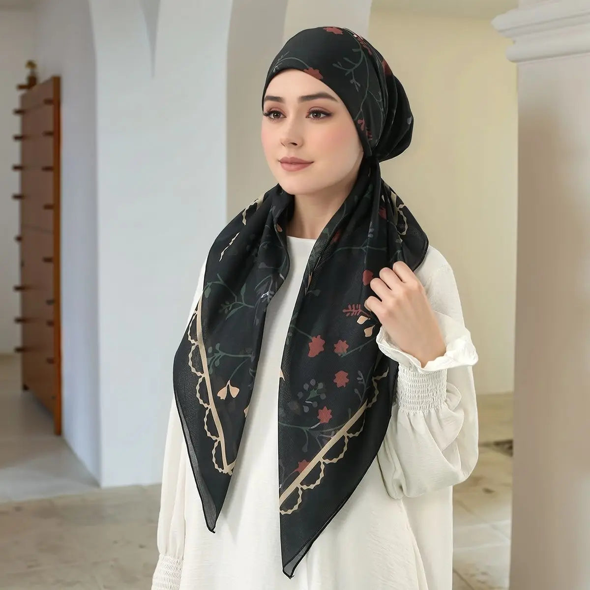 Eine Frau mit schwarzem floralem Voile-Hijab und weißem Oberteil.