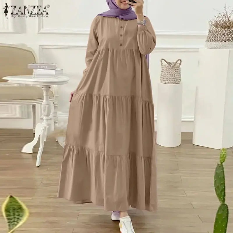 Eine Frau in einem langen, beigen muslimischen Kaftankleid mit lila Hijab drinnen.