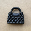 Un bolso de mano acolchado negro con asa mostrado contra un fondo neutro.