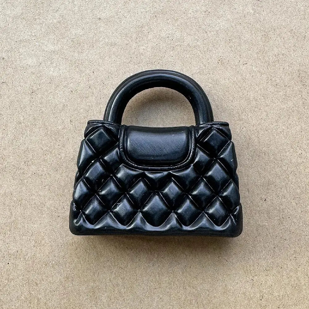 Un bolso de mano acolchado negro con asa mostrado contra un fondo neutro.