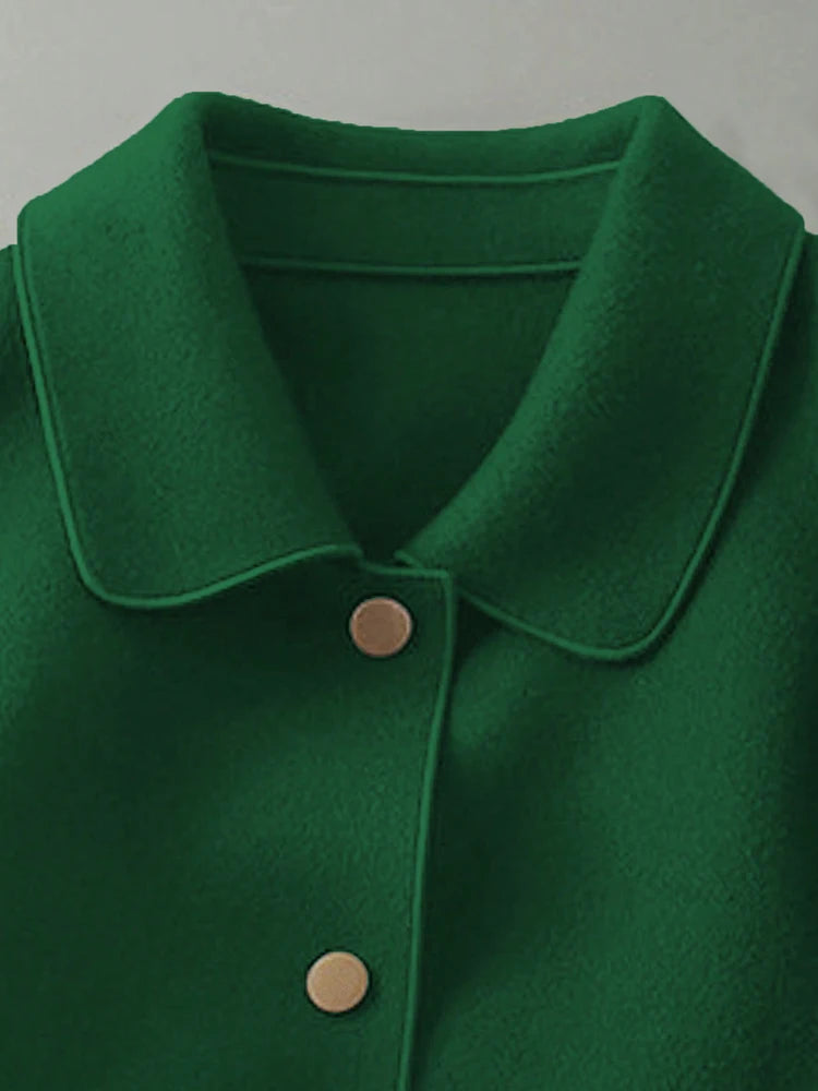 Gros plan d'un manteau en laine vert émeraude foncé à col et deux boutons visibles.