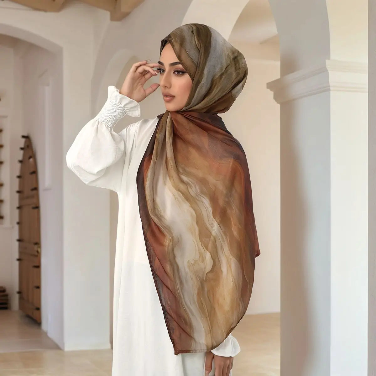 Eine Frau trägt einen braun-beige Aquarell-digitalen Hijab-Schal in einem weißen modesten Outfit.