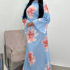A woman models a light blue abaya kaftan dress with a pink floral print against a white background.