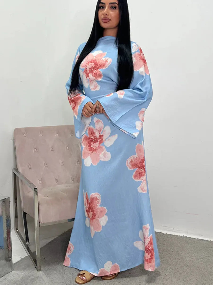 A woman models a light blue abaya kaftan dress with a pink floral print against a white background.