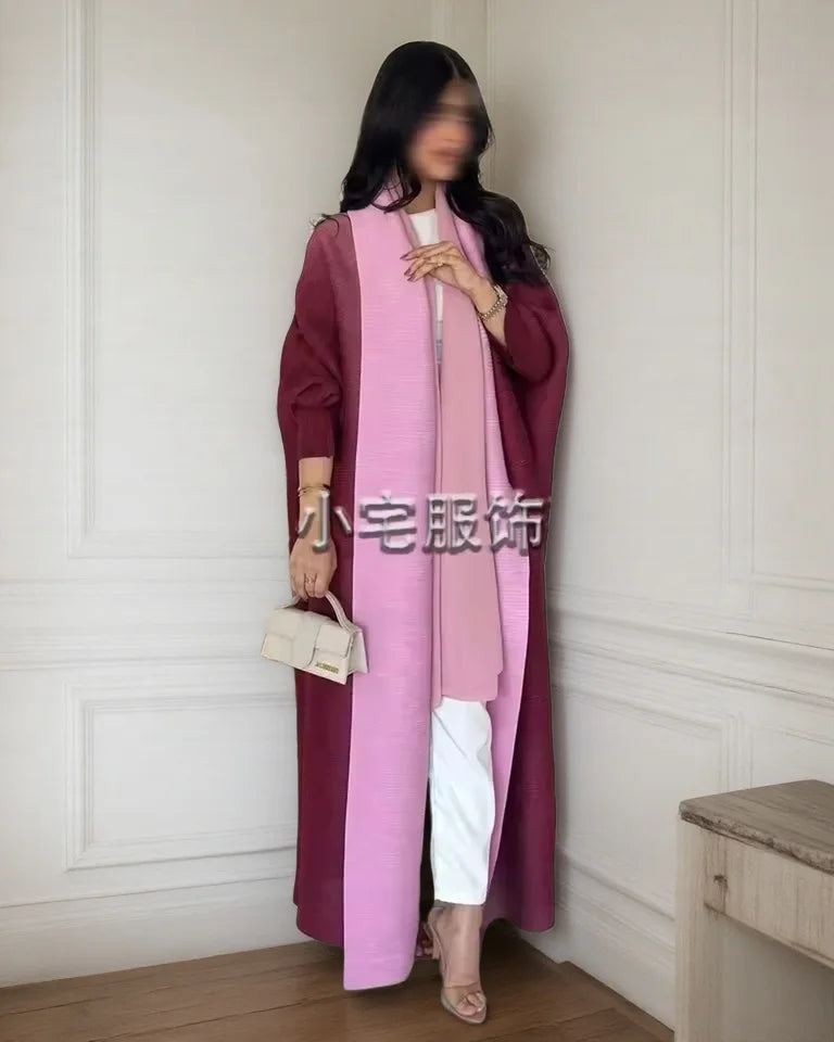 Una mujer modela un cárdigan largo de abaya plisado rosa sobre un vestido granate en una habitación bien iluminada.