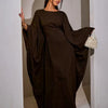 Modelo vistiendo una abaya de manga de murciélago marrón oscuro de lujo para noche, de pie en un arco blanco.