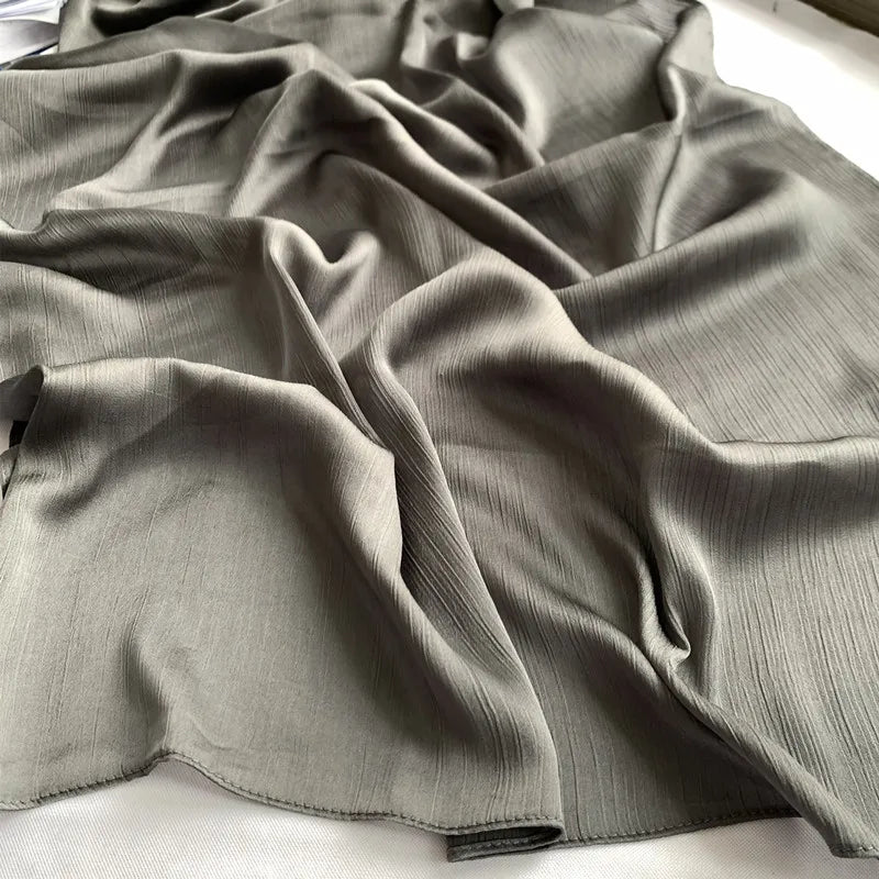 Ein Drapp von grauem gekräuseltem Satin-Chiffonstoff in einer fließenden, gefalteten Anordnung.