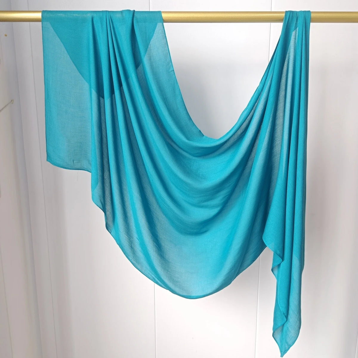 Foulard modal turquoise vif drapé sur un cintre.
