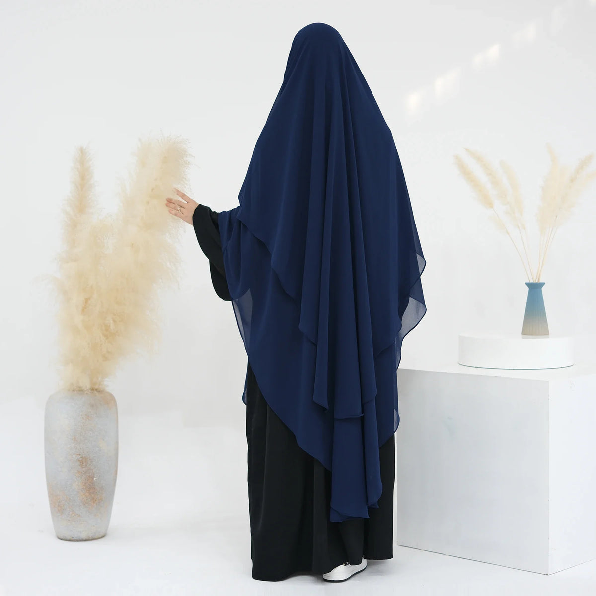 Eine Frau trägt einen dunkelblauen, zweilagigen Chiffon-Niqab und schwarze Kleidung vor weißem Hintergrund.