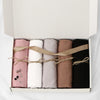 Une boîte contenant quatre foulards de hijab de couleur unie roulés en rose, blanc, beige et noir.