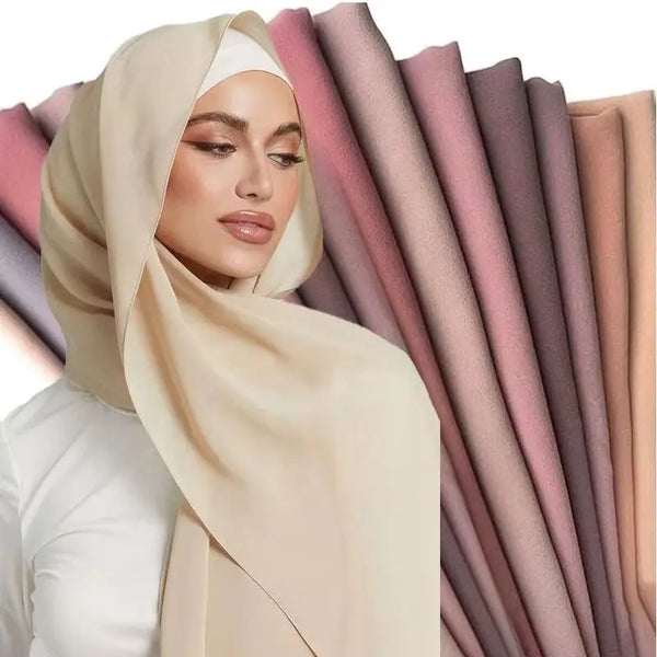 A woman wearing a beige chiffon hijab scarf against a background of vertically folded pink and mauve fabric.