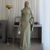 Eine Frau in einem eleganten, langärmeligen olivgrünen Hijab-Kleid steht in einem hellen Raum.