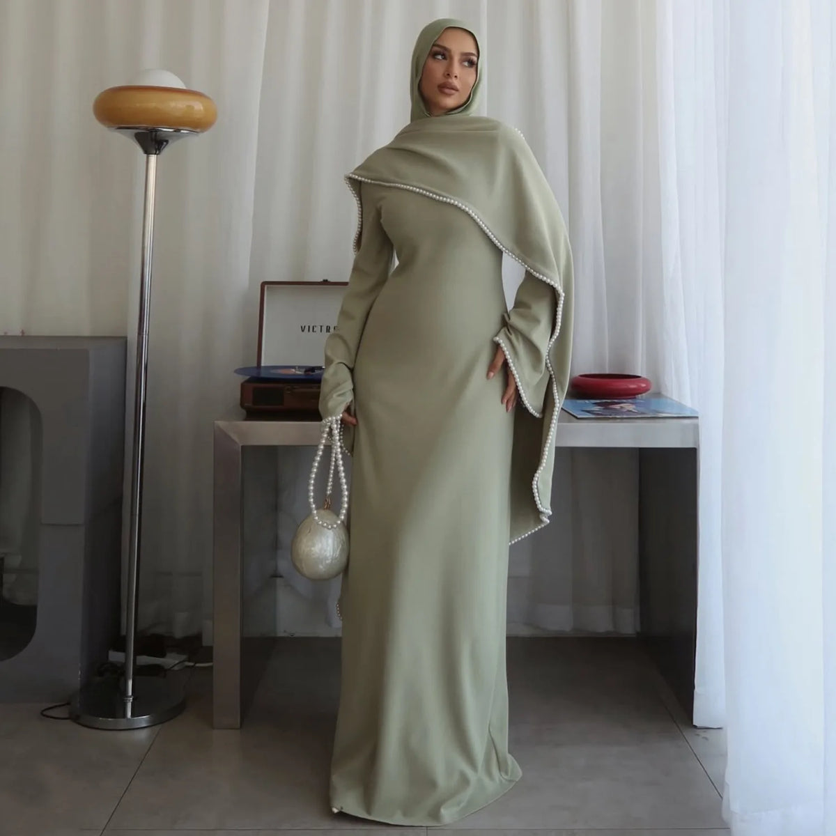 Eine Frau in einem eleganten, langärmeligen olivgrünen Hijab-Kleid steht in einem hellen Raum.