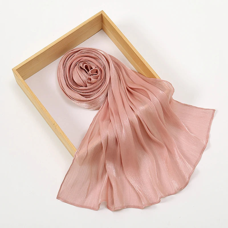 Un velo de chifón brillante color rosa polvoriento, drapeado elegantemente dentro de un marco de madera.