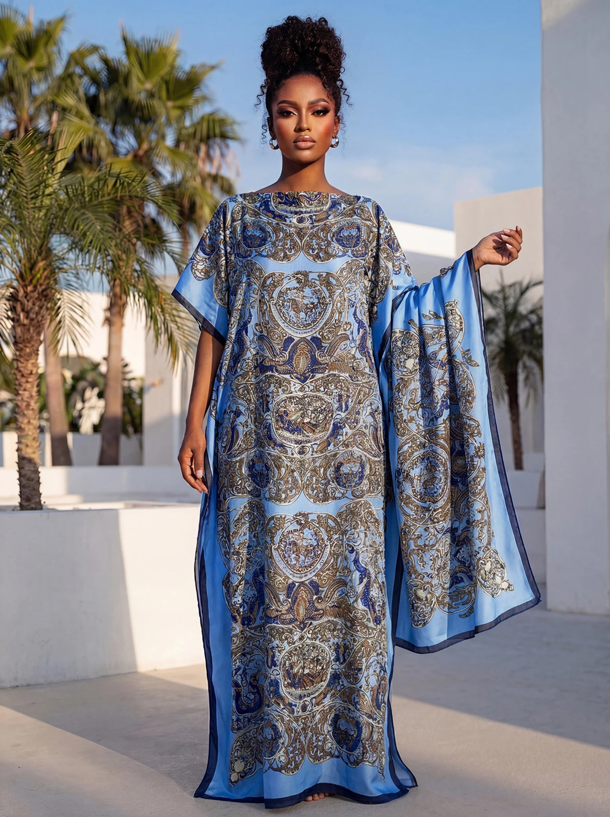 Eine Frau trägt ein elegantes bedrucktes Seidenkaftankleid in blau-goldenen Mustern im Freien.